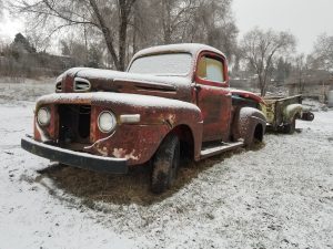 A rusty old truck is parked in the snow.