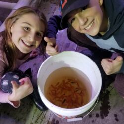 Two people sitting next to a large bucket of food.